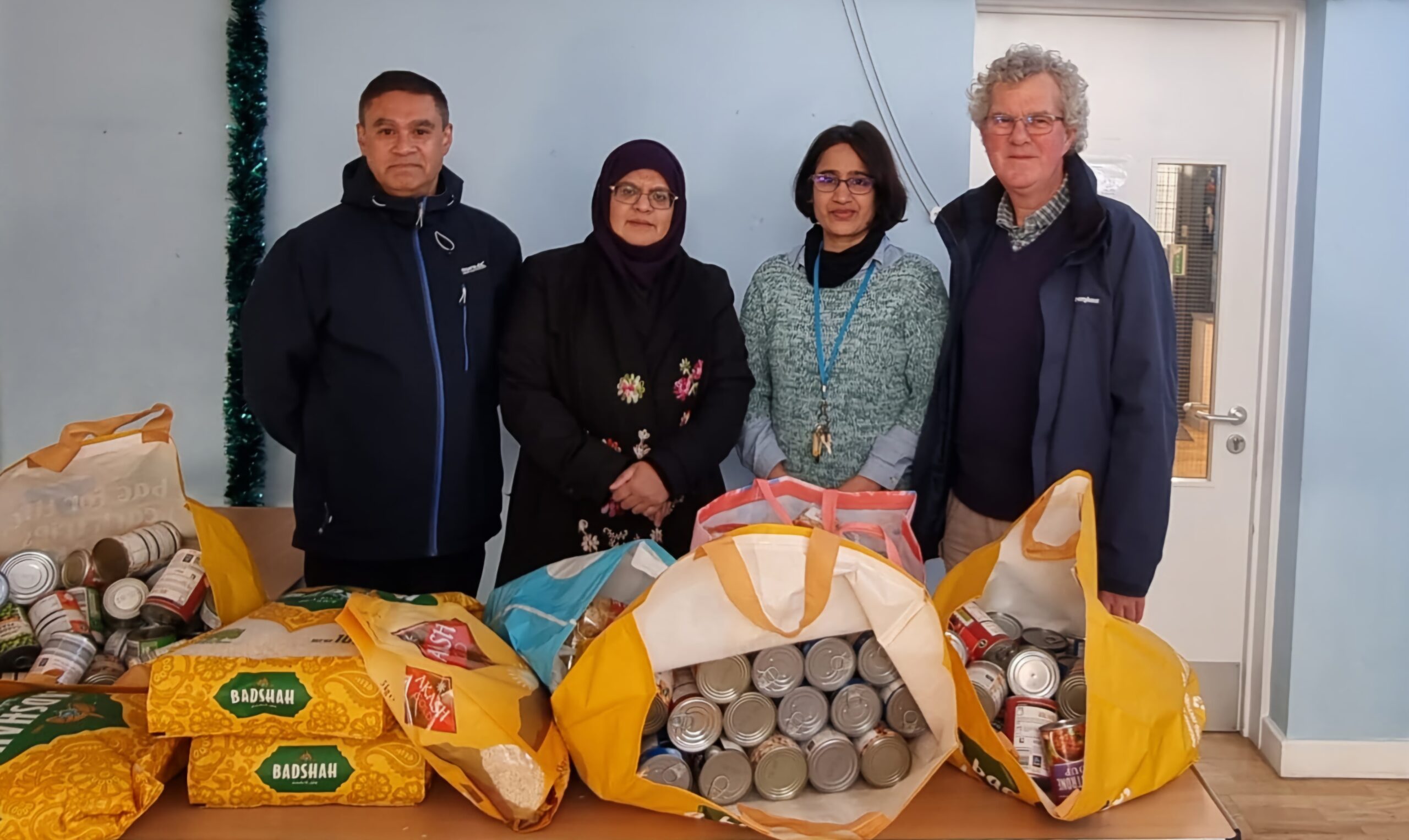 Kal Karim (far-left) and Shahida Rahman (second from left) with volunteers from the Trumpington Food Hub. They are all standing behind a table of essential food items donated by the Karim Foundation.