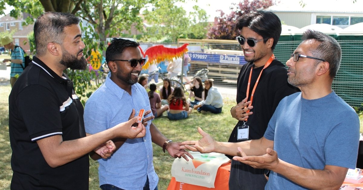 Four individuals engaged in a lively conversation with one holding a Karim Foundation keyring at the 2025 Arbury Carnival.